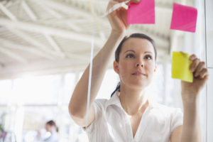 Beautiful young businesswoman putting adhesive notes on glass wall in office